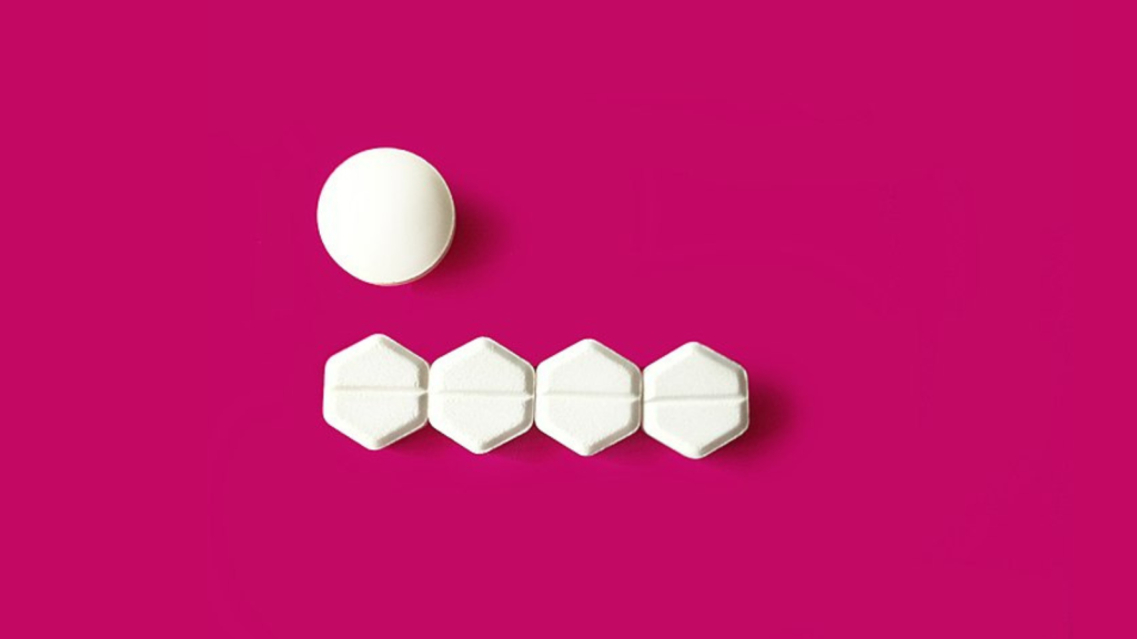 Pink background with one mifepristone pill and four misoprostol pills.
