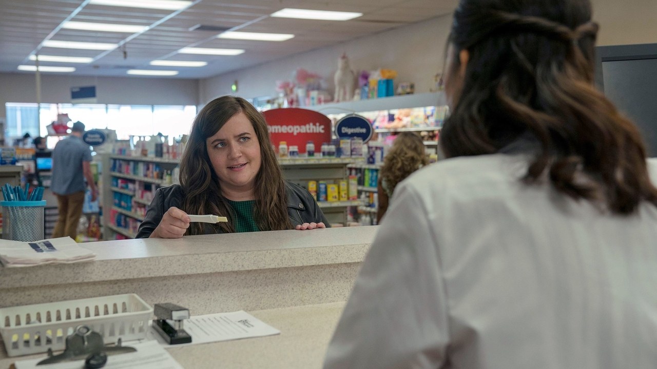 Shrill character Annie, played by Aidy Bryant, at pharmacy counter, holding pregnancy test